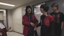 three men are standing in a hallway with one wearing a red jacket with the letter d on it