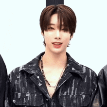 a man wearing a black jacket and a necklace looks at the camera