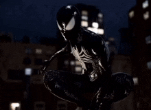 a spider man in a black suit is kneeling in the rain
