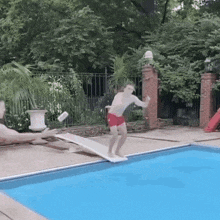 a man in red shorts is jumping into a swimming pool