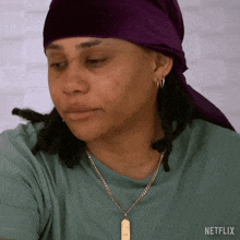 a woman wearing a purple head scarf and a necklace with netflix written on the bottom