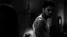 a man with a tattoo on his arm is wearing a tank top and looking at the camera .