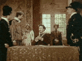 a group of men are standing around a table and one of them is wearing a crown