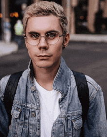 a man wearing glasses and a denim jacket is looking at the camera