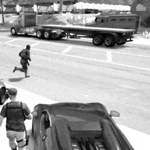 a black and white photo of a man running towards a truck with a flatbed trailer