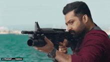 a man in a red shirt is holding a gun in front of a blue ocean