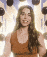 a woman in an orange tank top is smiling in front of balloons in the background