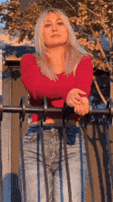 a woman in a red shirt and jeans is leaning against a railing .