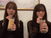 two girls drinking from glasses with straws in front of a picture