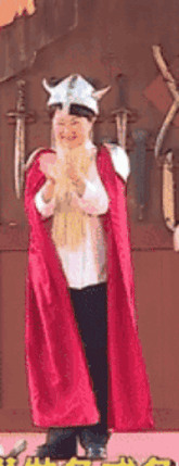 a man in a viking costume is standing in front of a wall with swords and shields .