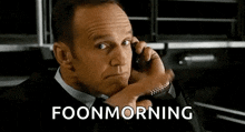 a man in a suit and tie is talking on a cell phone with the words `` foonmorning '' behind him .