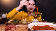 a woman in a yellow sweater is eating a sandwich with chopsticks