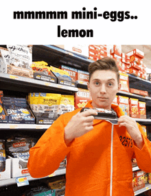 a man in an orange jacket is holding a candy bar in front of a sign that says " lemon "