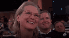 a woman wearing glasses is smiling while sitting next to a man in a tuxedo