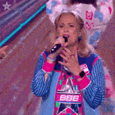 a woman singing into a microphone with a bbb shirt on