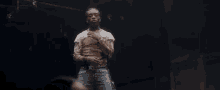 a man in a dirty shirt and jeans is standing on a stage in a dark room .