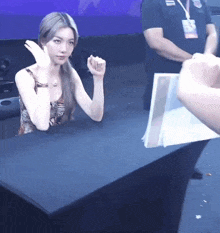 a woman sitting at a table with her fist in the air while a man holds a piece of paper in front of her