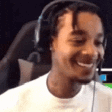 a man wearing headphones and a white shirt is smiling while sitting in a chair .