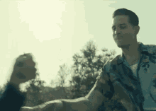 a man in a camouflage shirt is holding another man 's hand while standing in front of trees .
