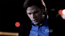 a man in a blue shirt and a black jacket is standing in the dark .