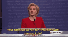 a woman in a red suit stands in front of a microphone and says " i will continue to run for president until "