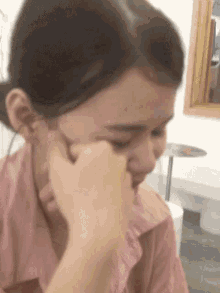 a woman in a pink shirt is covering her face with her hand .