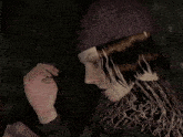 a woman wearing a knitted hat and scarf looks down at something