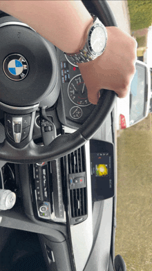 a person wearing a watch is driving a car with the bmw logo on the steering wheel