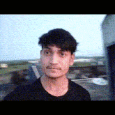 a young man is wearing a black shirt and looking at the camera .