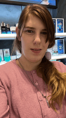 a woman wearing a pink sweater is standing in front of a display of biotherm cosmetics
