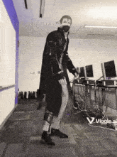 a man in a long black coat is standing in a room with a computer desk .