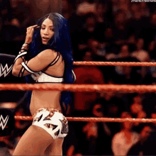 a woman with blue hair is standing in a wrestling ring with her hand on her head .