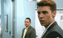 a man in a suit and tie stands in a hallway looking at the camera