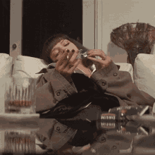 a woman is laying on a couch smoking a cigarette and drinking a glass of whiskey
