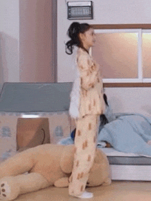 a girl in pajamas is standing next to a teddy bear in a bedroom .