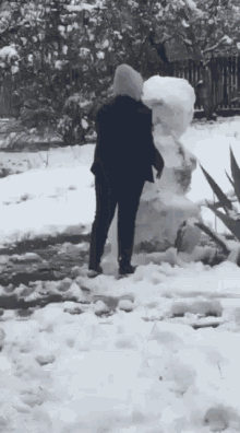 a person is standing in the snow near a large snowman