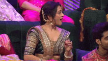 a woman in a sari is sitting on a couch with her mouth open
