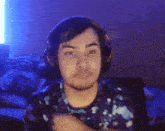 a man wearing headphones and a blue shirt is sitting in front of a blue light .