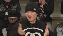 a man wearing a black beanie and a ny sweatshirt is clapping his hands