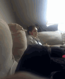 a woman sits on a couch in front of a window eating a snack