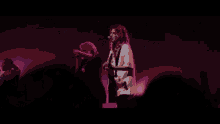 a woman singing into a microphone while holding a guitar in front of a crowd