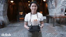 a woman is holding a tray of food and the word delish is on the bottom