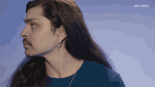a man with long hair and a mustache is wearing a blue sweater with the elite daily logo behind him