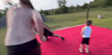 a woman and a child are playing on a red mat in a park .