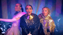 three women are standing next to each other on a stage and one of them is wearing a gold necklace