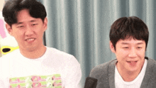 two men are sitting next to each other in front of a microphone .