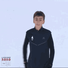 a young boy stands in front of a sign that says lausanne 2020 youth olympic games