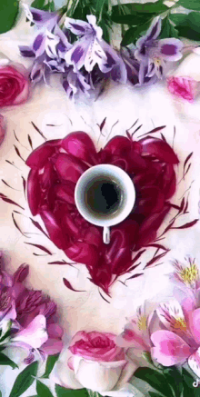 a cup of coffee is sitting in the middle of a heart made of petals surrounded by flowers .