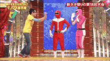 a man in a yellow shirt stands next to a man in a red suit and a woman in a pink outfit