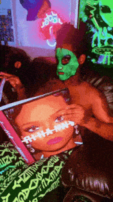 a man wearing a green mask is reading a magazine next to a woman wearing a mask .